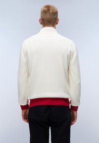 Cremfarbener Pullover mit rot geripptem Saum und Bündchen, ausgestattet mit einem hohen Kragen und einer Strickstruktur. Schlichte, entspannte Silhouette.