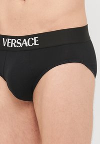 Mustadest puuvillast aluspüksidest, millel on pehme vööka ning valgete tähtedega "VERSACE". Disain on sobiv ja sujuva tekstuuriga, millel on minimaalsed õmblused.