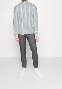 Lichtblauw en beige gestreept overhemd met lange mouwen en een opstaande kraag, gecombineerd met donkergrijze taps toelopende broek en witte sneakers. Gladde stoftextuur.