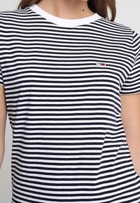 Camiseta de rayas en azul marino y blanco, de manga corta, con cuello redondo y un ribete blanco, presenta un pequeño logo en el pecho.