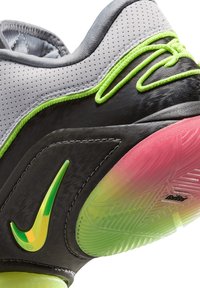 Zapatilla deportiva gris con detalles verdes, parte superior texturizada, media suela negra y suela multicolor con detalles en rojo y amarillo. Se muestra el logo de Nike.