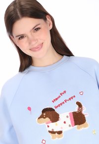 Világoskék pulóver texturált, hímzett kutya mintával. Játszós szöveggel és színes, ünnepi díszítésekkel kísérve.