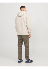 Sudadera beige claro con capucha ajustable, combinada con pantalones cargo verde oliva. Zapatillas azules completan el conjunto.