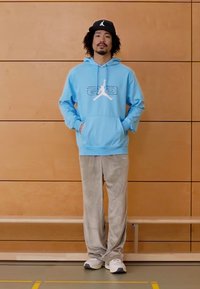 Sweatshirt com capuz azul claro com logótipo gráfico branco, combinada com calças cinzentas aveludadas e sapatilhas brancas desportivas. Design simples, corte descontraído.