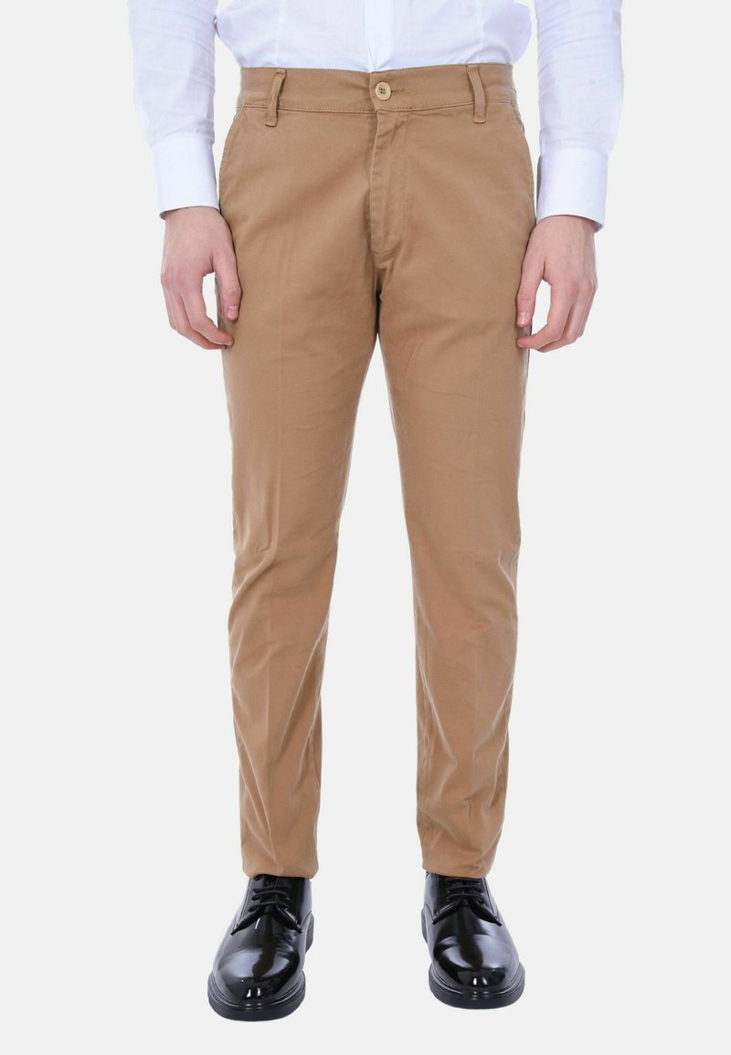 Pantaloni chino color khaki, slim fit, in cotone con tasche frontali e chiusura a bottone. Abbinati a scarpe eleganti nere e lucide.