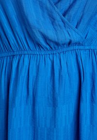 Zila kleita no teksturētas auduma, ar savāktu jostu ar elastīgu piešuvumu un vertikālām svītrām dažādos zilās krāsas toņos.