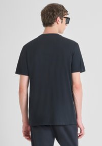 Camiseta de algodón negro con cuello redondo y manga corta, que presenta un ajuste holgado y una textura suave, mostrada desde la parte de atrás.