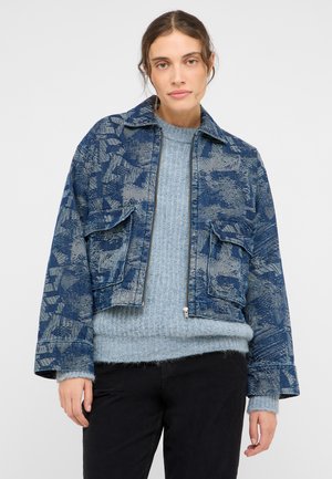 Cropped blue denim jacket with a patterned texture, zip closure, and two front pockets worn over a light blue knitted sweater.