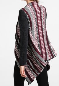 Stickad cardigan med ett mönster i vinrött, vitt och svart, långa ärmar och en asymmetrisk fåll.