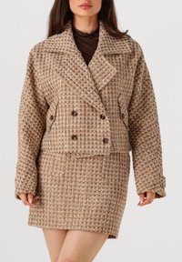 Bruine tweed dubbelbreasted jas met grote revers, gestructureerd patroon en voorzakken, gecombineerd met een bijpassende getailleerde rok.