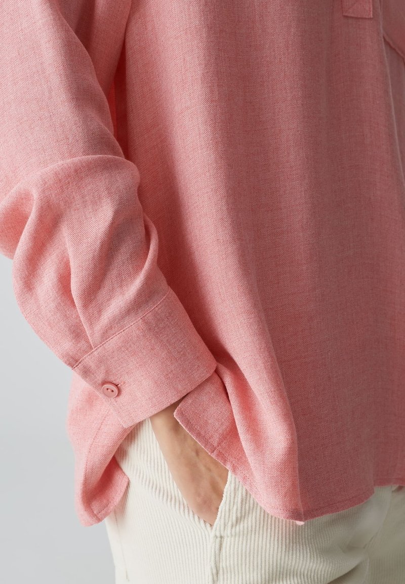 Helles rosa Langarmshirt aus strukturiertem Stoff. Verfügt über eine knöpfbare Manschette und eine lockere Passform, die ein dezentes gewebtes Muster präsentiert.