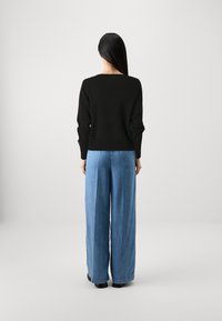 Svart tröja med avslappnad passform, ribbad nederkant, i kombination med högmidjade ljusblå vida jeans. Mjuk textur, minimalistisk design.