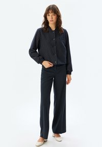 Marine-stribet knappet jakke i et blødt materiale med en cropped design, parret med matchende brede bukser og lyse sko.