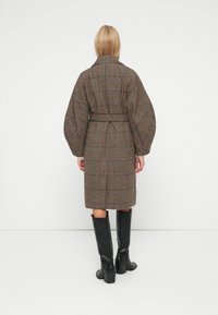 Kabát s kostkovaným vzorem houndstooth, s páskem v pase, balónovými rukávy a límcem. V kombinaci s černými kozačkami po kolena na bílém pozadí.