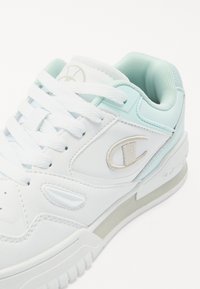 Sneaker bianco con accenti azzurri, realizzato in materiale sintetico. Presenta un colletto imbottito, lacci bianchi e un sottile dettaglio del logo.