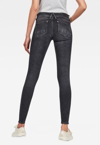Jeans ajustados de denim gris oscuro con una textura suave, cintura de altura media y bolsillos traseros; combinados con zapatillas de color claro.