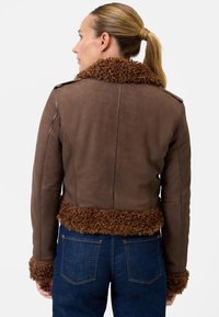 Brun läderjacka med lockigt brunt fårskinnskrage och ärmslut, figurnära design och sömmar på ryggen, kombinerad med mörkblå jeans.