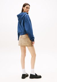 Blå hettegenser med senkede skuldre, kombinert med en beige denim miniskjørt. Sorte loafers og hvite ankelsokker fullfører antrekket.