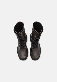 Brown leather lace-up boots with a high shaft, textured black rubber sole, and side zipper detail. Features metal eyelets and dark laces.