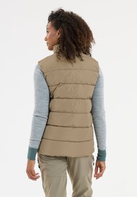 Beige Puffer-Weste mit horizontaler Naht, hohem Kragen und einer glatten Textur. Darunter ein hellblaues Langarmhemd mit einem Manschettenakzent.