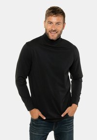 Schwarzes Rollkragenshirt aus weichem Stoff, mit langen Ärmeln und einer taillierten Passform, kombiniert mit blauen Jeans.