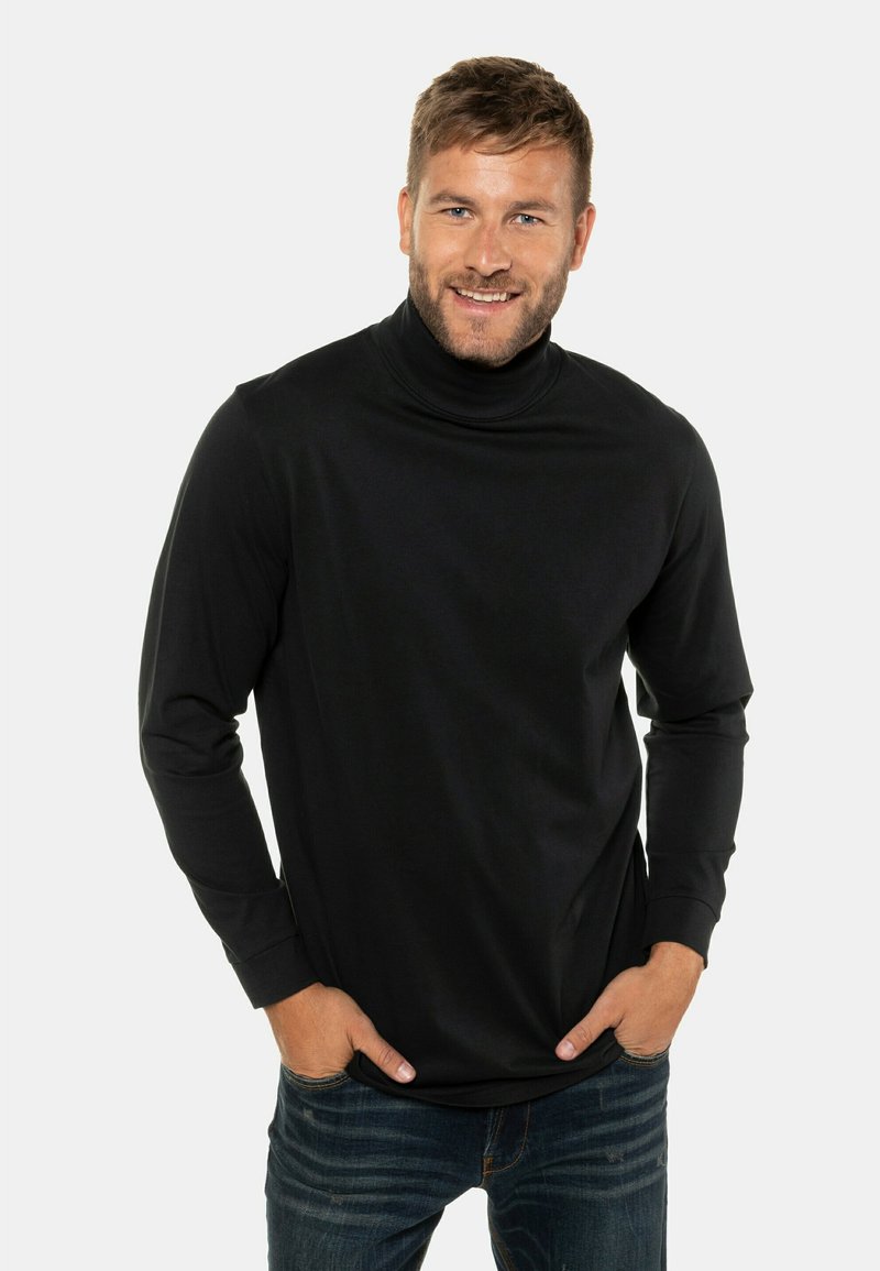 Schwarzes Rollkragenshirt aus weichem Stoff, mit langen Ärmeln und einer taillierten Passform, kombiniert mit blauen Jeans.