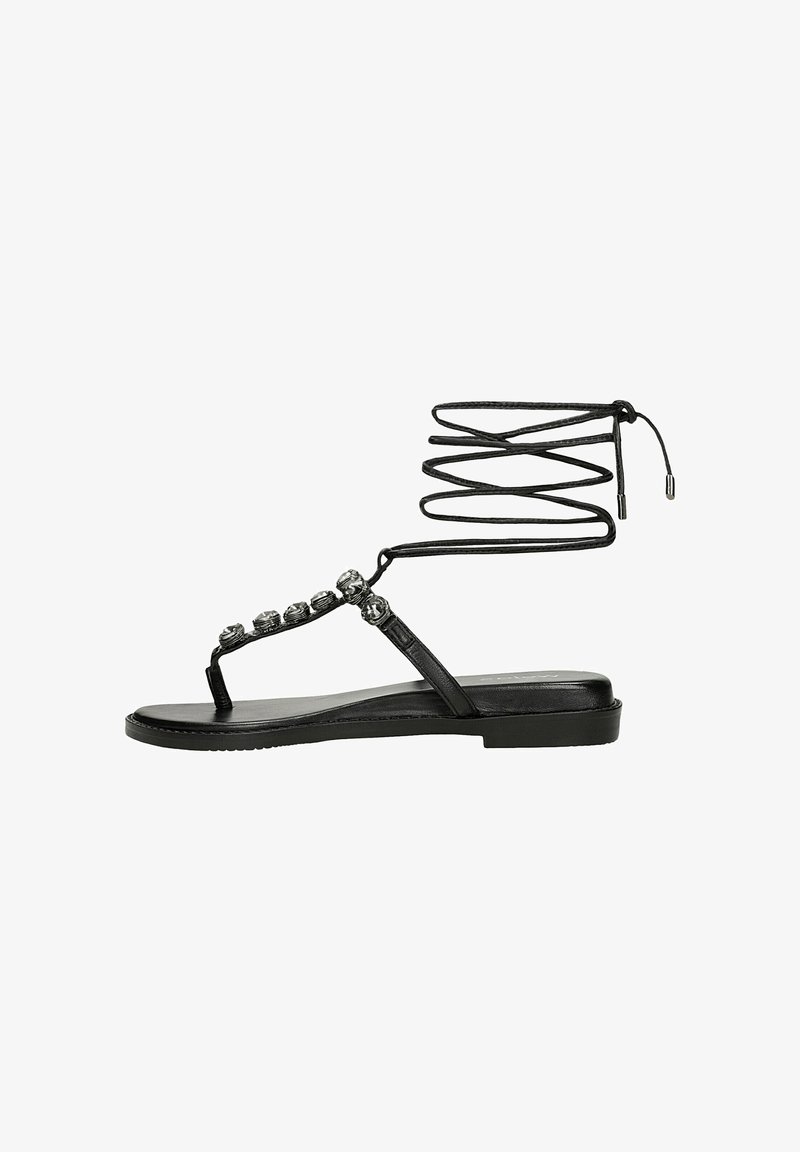 Sandali piatti neri con una fascia sulla suola e dettagli metallici decorativi. Presentano un design a lacci avvolgenti attorno alla caviglia. Texture liscia.