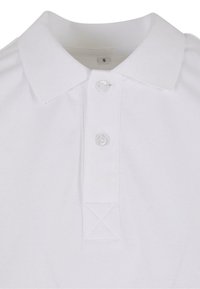Hvit polo skjorte med kragehals, tre knapper foran og strukturert stoff. Har broderte detaljer ved kragen og kanten.