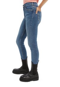 Jeans de denim azul ajustados con una cintura de altura media, dos bolsillos frontales y botas negras hasta el tobillo con suela gruesa y paneles elásticos en los laterales.