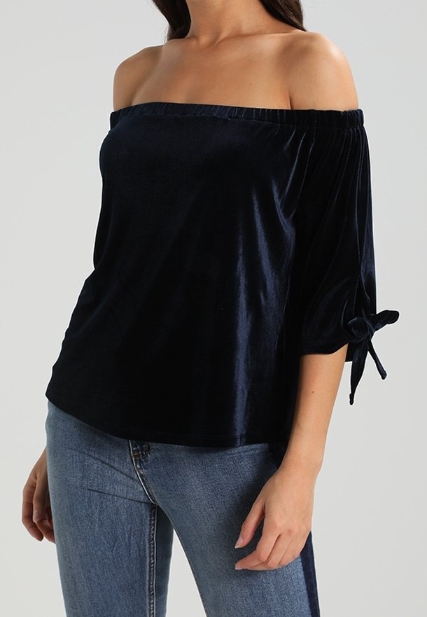 Marinblus utan axlar i sammetsliknande tyg, med trekvartsärmar med knytningar. Slät textur och avslappnad passform.