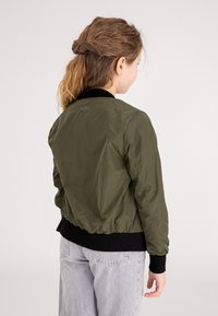 Olijf groene bomberjack met een gladde textuur, ribgebreide zwarte manchetten en tailleband, en subtiele geborduurde details op de achterkant.