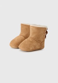 Tan mockasiner med ett mjukt vitt ullfoder, med en kort design och en dekorativ rosett på sidan, lämpliga för kallare väder.