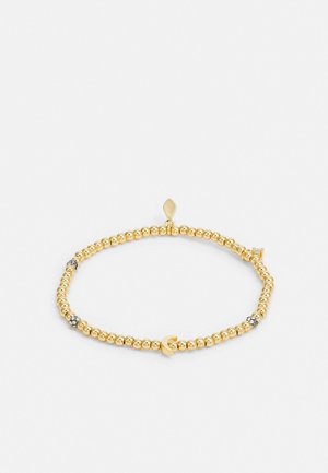 Złota bransoletka z koralikami, z małym serduszkiem i koralikami przypominającymi diamenty, z zawieszką w kształcie diamentu na białym tle.