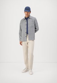 Knappe skjorte i et blått og hvitt rutemønster, brukt over en marineblå topp, med beige bukser og hvite sneakers. Inkluderer en blå caps.