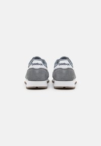 Zapatillas deportivas de ante gris con marca blanca, una silueta redondeada y una lengüeta texturizada en gris. Cuenta con una entresuela blanca y suela en tono marrón.
