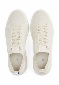 Zapatillas beige claras con una parte superior de malla texturizada, cordones planos y suela de goma. Presenta un logotipo en el lateral y un forro suave.