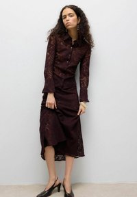 Pitsist burgundiapunane pluus nööpkinnitusega ja lehvikukujuliste varrukatega, sobitatud vastava pitsseelikuga ja mustade trakslinga kontsakingadega.