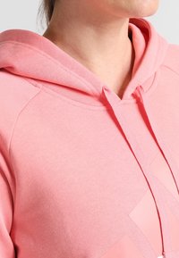 Ljusrosa hoodie gjord av bomullsblandat material. Har en dragsko i huvan och ett diamondmönster framtill, med ribbade detaljer.