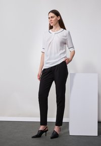 Blouse blanche avec bordure noire, manches courtes et plis, assortie à un pantalon noir ajusté et des escarpins noirs à bout pointu. Design simple et épuré.