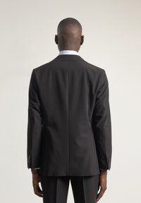 Chaqueta de traje negra con un corte ajustado, que presenta una abertura sencilla, mangas largas y botones en los puños; tejido suave con un acabado mate.