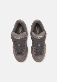 Mørk grå semsket sneakers med gummisåle, med teksturerte snørebånd og et logo-patch på tungen. Enkel, lavprofil design.