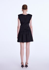 Robe noire à silhouette ajustée, avec de courtes manches raglan et une taille plissée. La jupe présente un design froncé pour plus de volume. Fermeture éclair dans le dos.