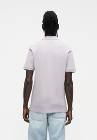 Polo grigio chiaro con colletto classico e maniche corte. Il tessuto appare liscio, abbinato a jeans azzurri.