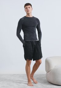 Čierna košeľa s dlhým rukávom, priliehavým strihom a textúrovanou tkaninou, kombinovaná s čiernymi šortkami vo voľnejším strihu s gombíkovými detailmi.