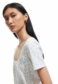 Blusa floreale con maniche corte, realizzata in tessuto leggero. Presenta un morbido scollo a girocollo, uno sfondo bianco e delicati motivi pastello.