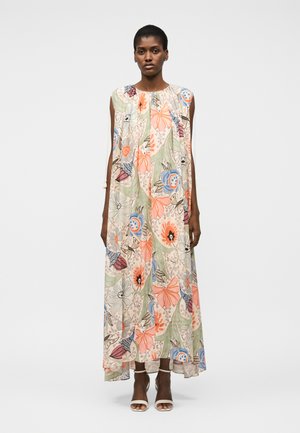 Γυναίκα που φοράει φόρεμα χωρίς μανίκια μέχρι τον αστράγαλο με πορτοκαλί, μπλε και πράσινα λουλουδένια μοτίβα, σε συνδυασμό με λευκές ανοιχτές γόβες.