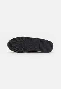Sneaker nera con una suola in gomma testurizzata caratterizzata da un motivo di battistrada ondulato. Il materiale superiore sembra essere tessuto con una finitura liscia.