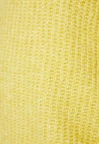 Detailní záběr na měkkou, načechranou žlutou pleteninu s vertikální strukturovanou texturou.