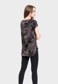 Camo print t-shirt in shades of gray and black, loose fit, short sleeves, slightly longer back, paired with black leggings.