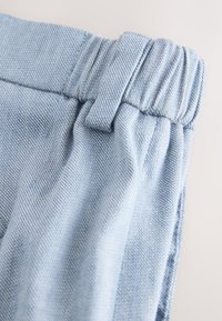 Light blue denim fabric with an elastic waistband and a belt loop, showing detailed stitching and texture.